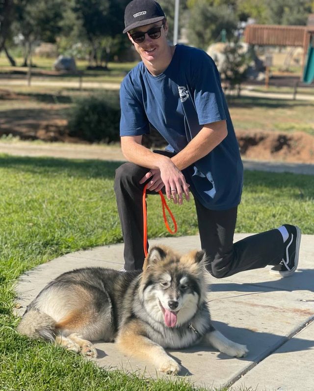 A trainer kneeling beside a husky malamute mix during leash training in a San Diego park